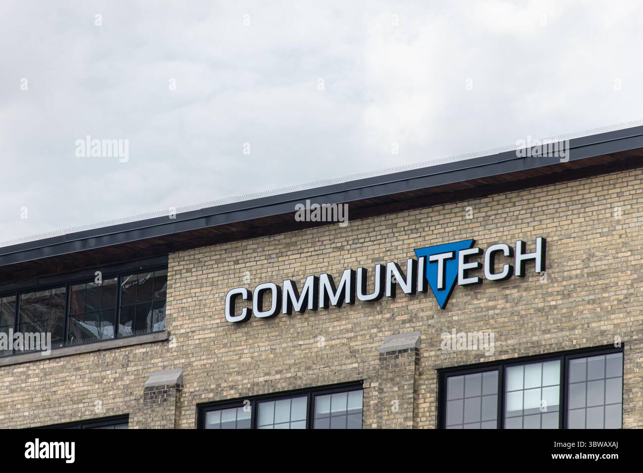 Primo piano del logo Communitech sulla facciata storica in mattoni sotto il cielo coperto, simboleggiando l'innovazione tecnologica a Kitchener. Foto Stock