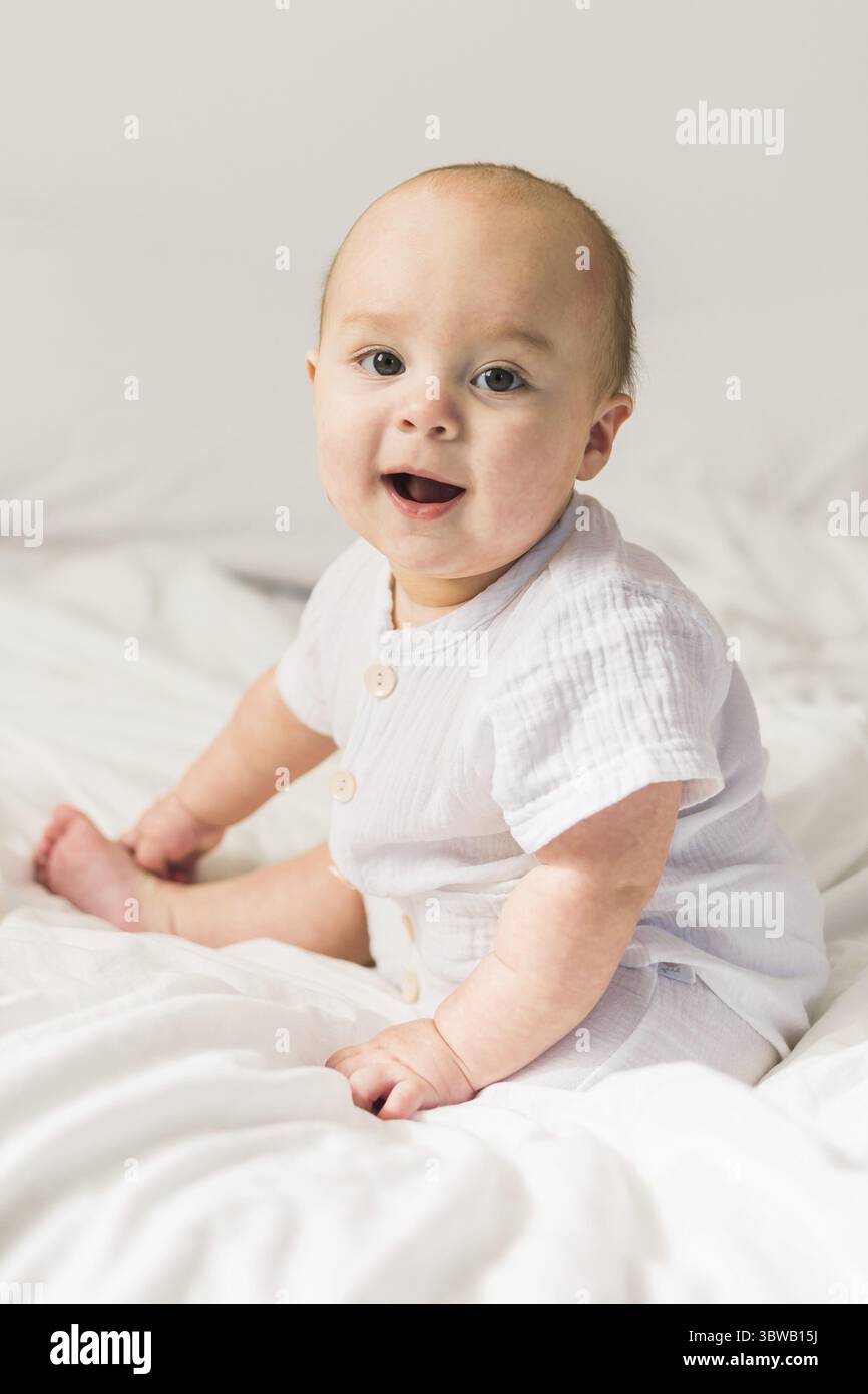 Laechelndes Neugeborenen auf einem weissen Bett zu Hause, das Konzept eines gluecklichen gesunden Saeuglings. Erzeugung alpha und gen alpha Foto Stock