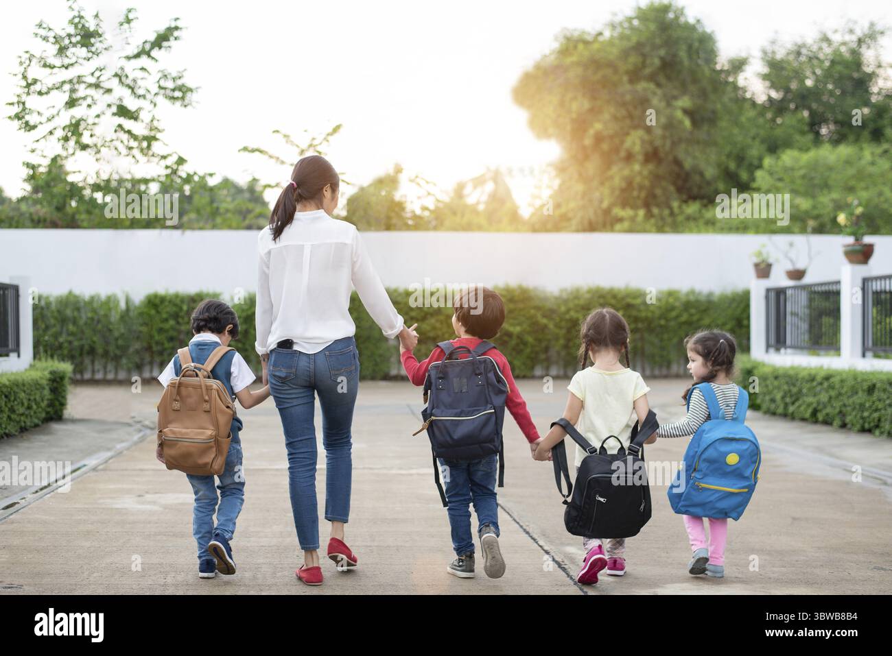 Gruppo di studenti in età prescolare e docente in possesso di mani e piedi a casa. La mamma di portare i suoi bambini vanno a scuola insieme. Si torna a scuola e istruzione c Foto Stock