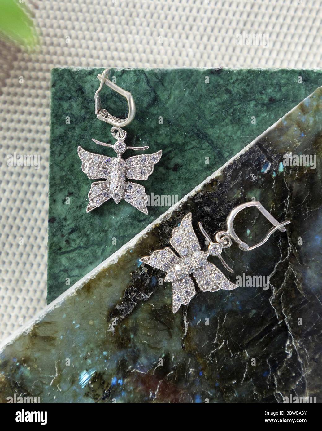 Un paio di orecchini a farfalla in argento adornati da scintillanti cristalli sono adagiati su una lastra di marmo verde Foto Stock