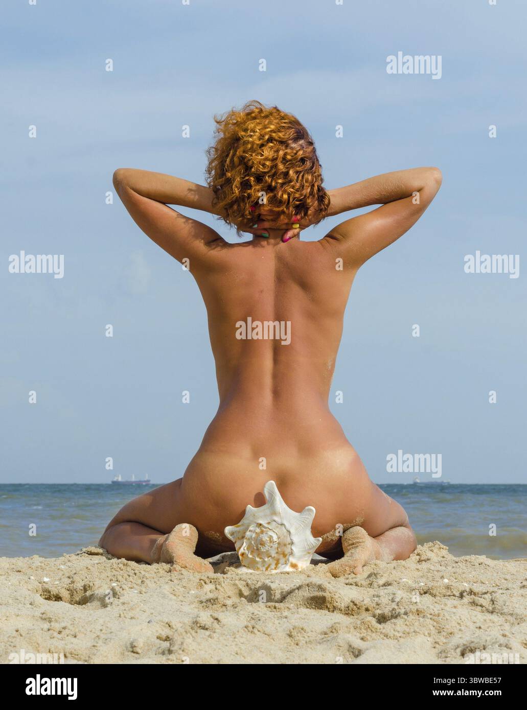 Giovane donna dai capelli rossi abbronzata seduta su una grande conchiglia in riva al mare Foto Stock