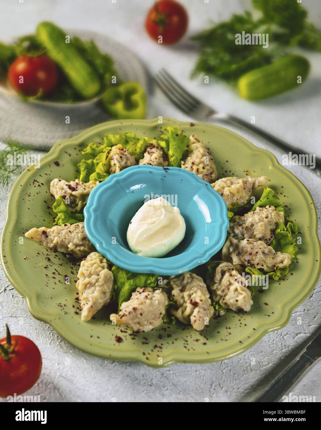 Gnocchi di manti al vapore conditi con fiocchi di pepe rosso serviti su un piatto verde con panna acida, un punto fermo della cucina dell'asia centrale Foto Stock