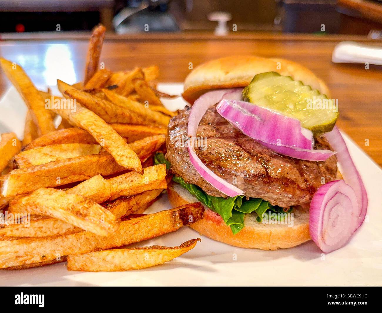 Vista ravvicinata di un succulento hamburger con patatine fritte tagliate a mano, cipolla e cetriolo su un panino fresco Foto Stock