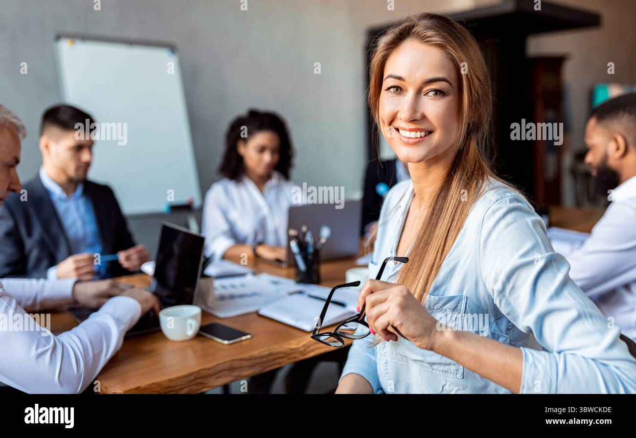 Donna d'affari sorridente seduta in riunione con i colleghi in ufficio Foto Stock