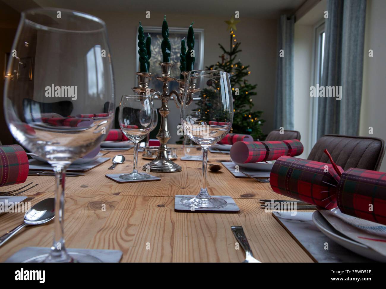Tavolo da pranzo festivo con bicchieri e cracker natalizi in una sala accogliente con un albero decorato e candele Foto Stock