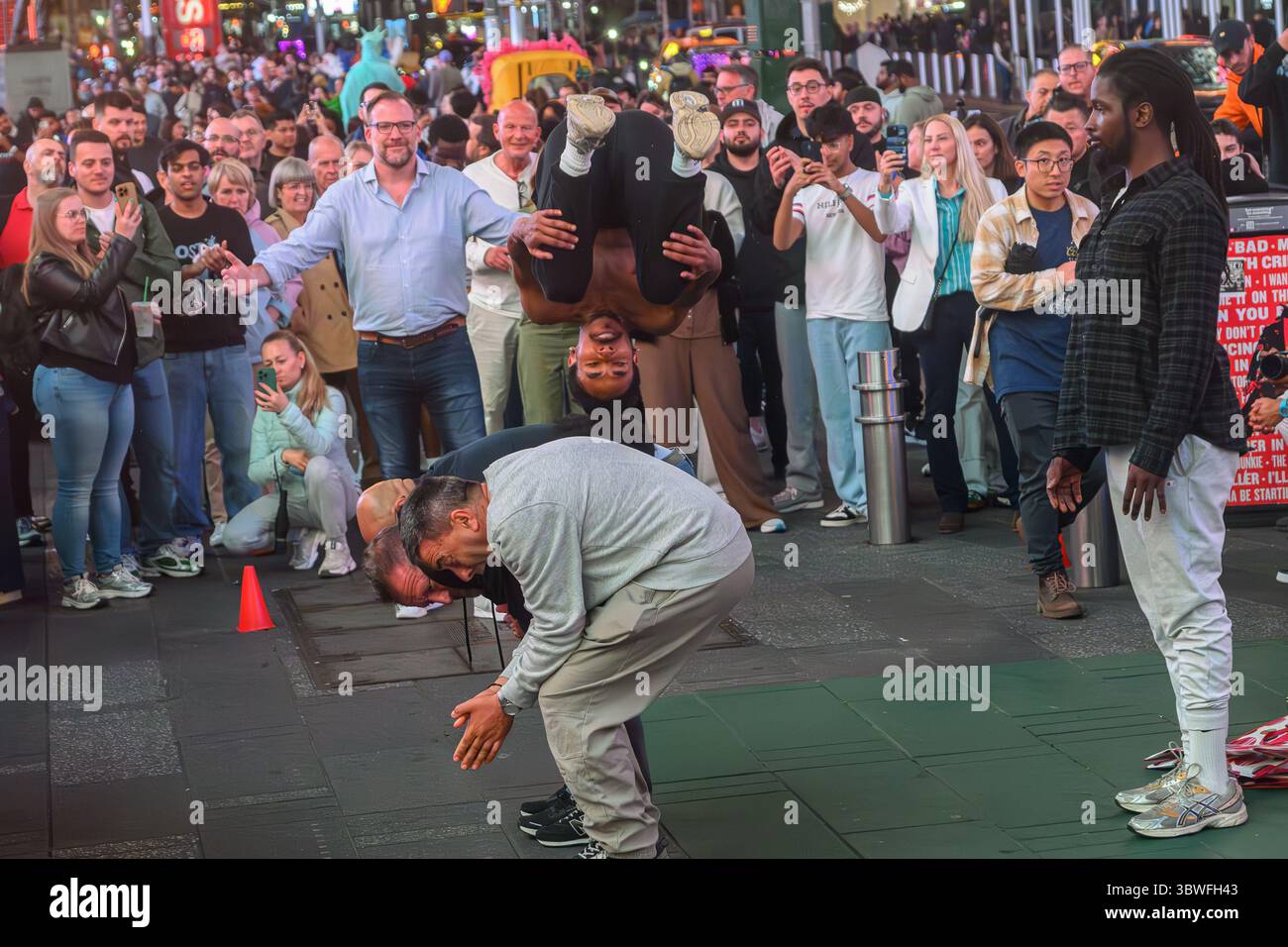 Un Performer intrattiene un pubblico di Somersaulting sui membri del pubblico partecipanti, alcune riprese su telefoni cellulari, a Times Square New York. Foto Stock