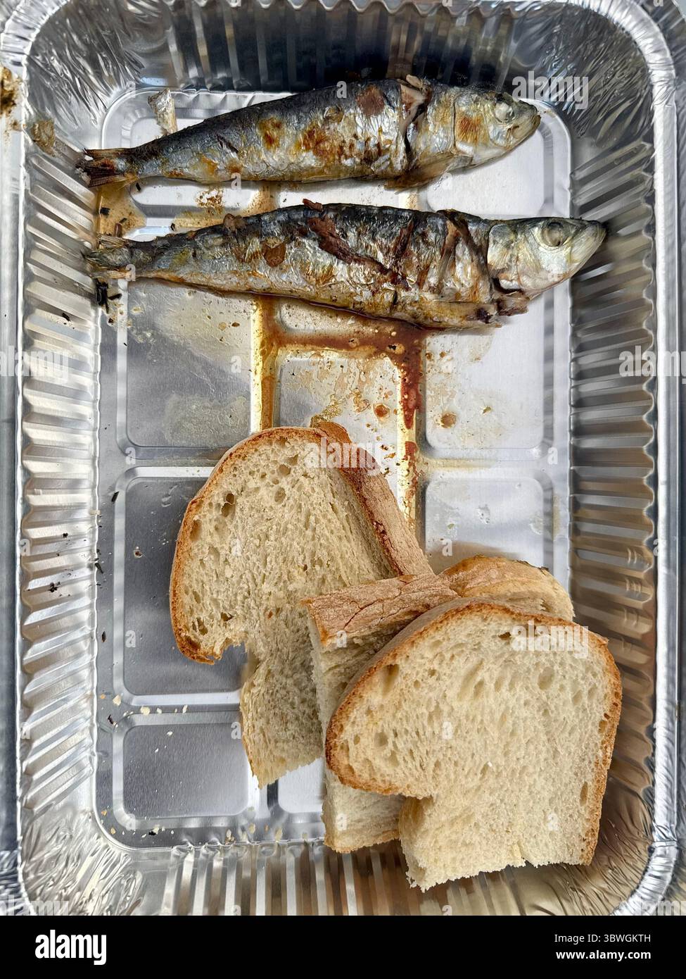 Sardine alla griglia servite con fette di pane in un vassoio di alluminio, cibo tradizionale portoghese di strada. - Immagine stock catturata con smartphone
