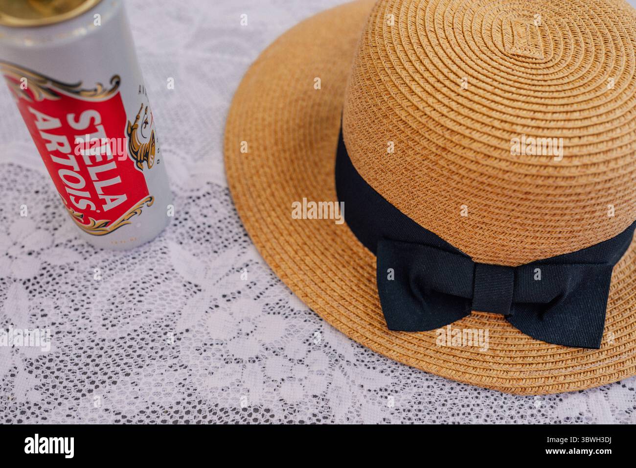 Lattina di birra Stella Artois in tavola con tovaglia in pizzo bianco e cappello di paglia con fiocco Foto Stock