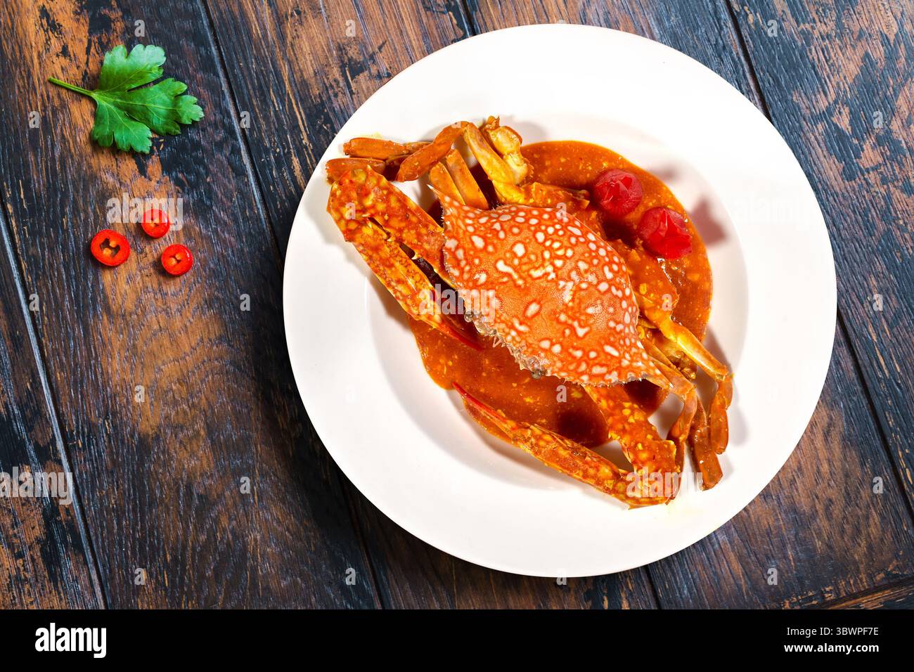 Delizioso curry di granchio servito su un piatto bianco, ricco di spezie e colori vivaci, guarnito con peperoncino rosso ed erbe aromatiche. Una miscela perfetta di sapori di pesce Foto Stock