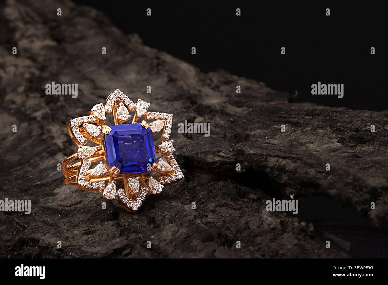 Questo squisito anello in oro presenta un audace zaffiro blu al centro, incorniciato da scintillanti dettagli diamantati in un motivo floreale. Una miscela perfetta di ele Foto Stock