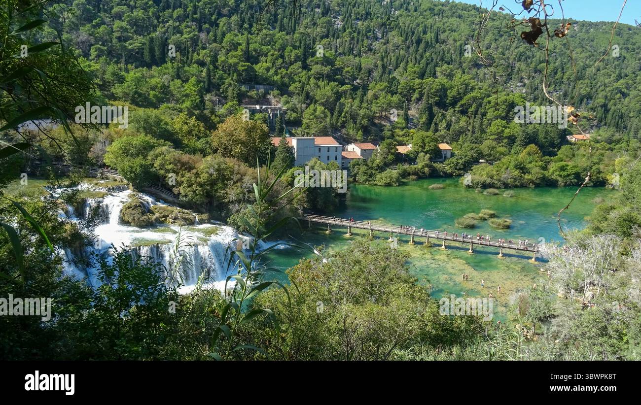 Vista dall'alto della cascata Skradinski Buk e della passerella in legno nel Parco Nazionale di Krka, Croazia, circondata da foresta e acqua color smeraldo con i visitatori che si divertono Foto Stock