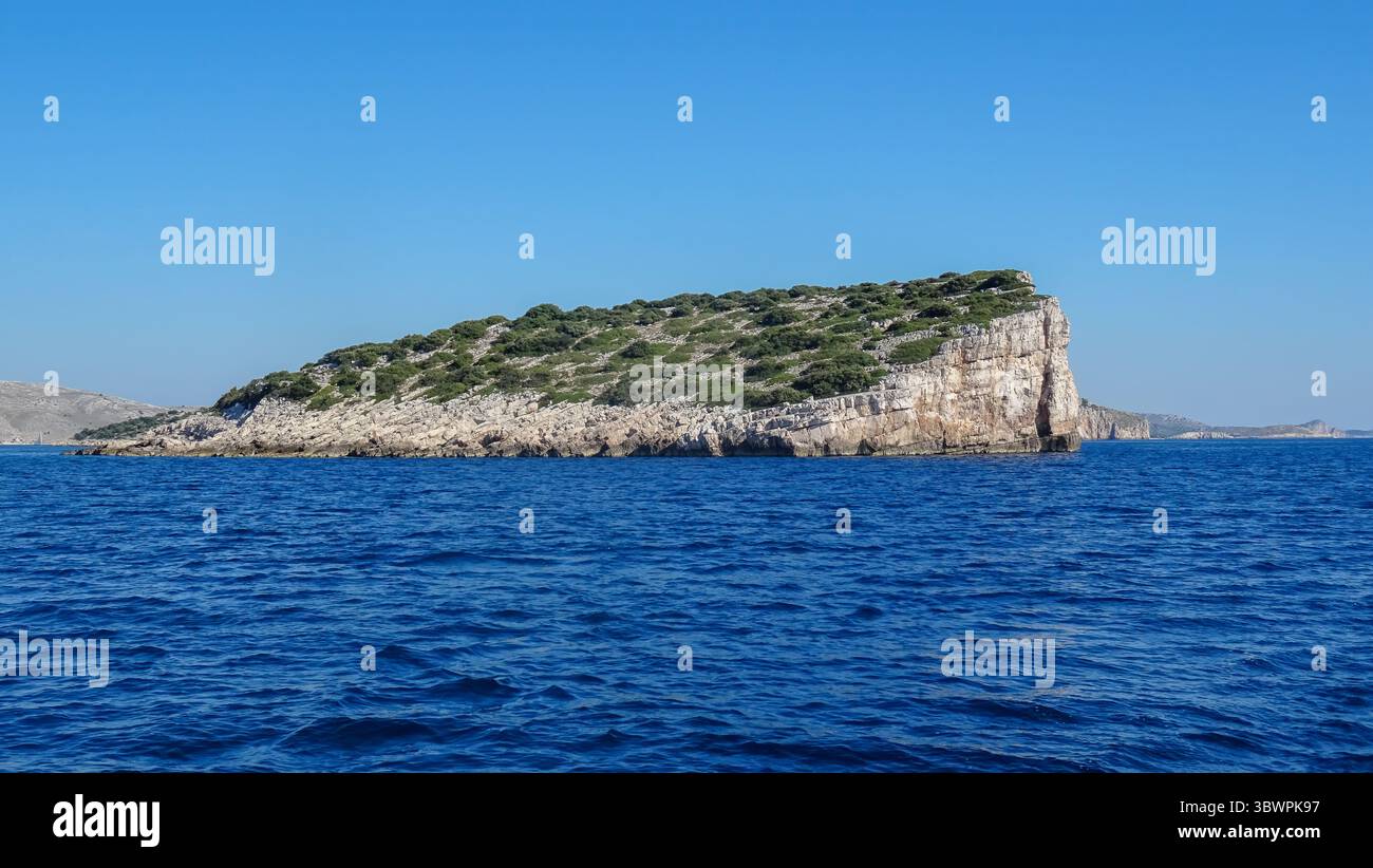 Isola rocciosa con scogliere ripide e vegetazione sparsa nell'arcipelago di Kornati, circondata dal blu profondo del mare Adriatico sotto il cielo estivo. Foto Stock