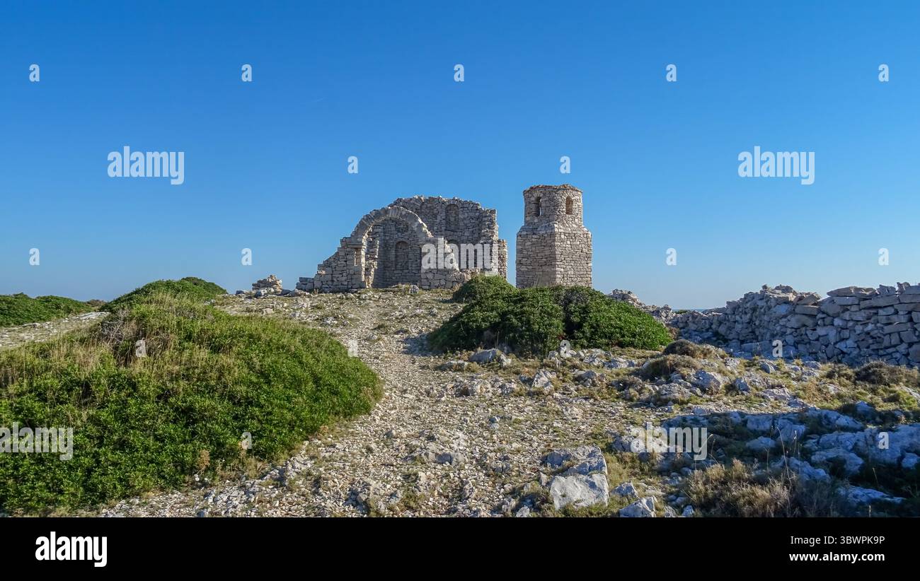 Rovine di un'antica chiesa in pietra con un arco e un campanile conservati su una collina rocciosa nel Parco Nazionale di Kornati, in Croazia, sotto un cielo blu brillante. Foto Stock