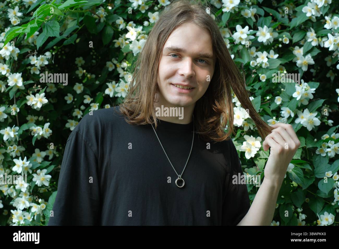 Un individuo allegro gioca con i capelli in un giardino pieno di fiori fioriti. Foto Stock