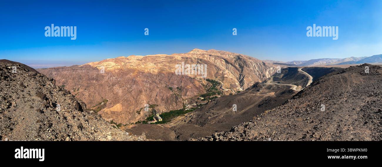 Vista panoramica delle aspre montagne desertiche vicino a Dhiban, al Governatorato di Madaba, in Giordania, con una strada tortuosa e una valle profonda sotto il cielo azzurro. Foto Stock