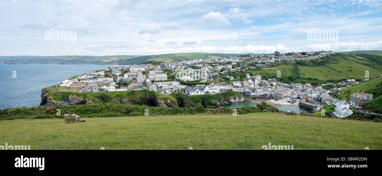 port isaac, inghilterra, 22 giugno 2025: coppia in panchina al punto panoramico sopra il porto e il villaggio di port isaac in cornovaglia Foto Stock