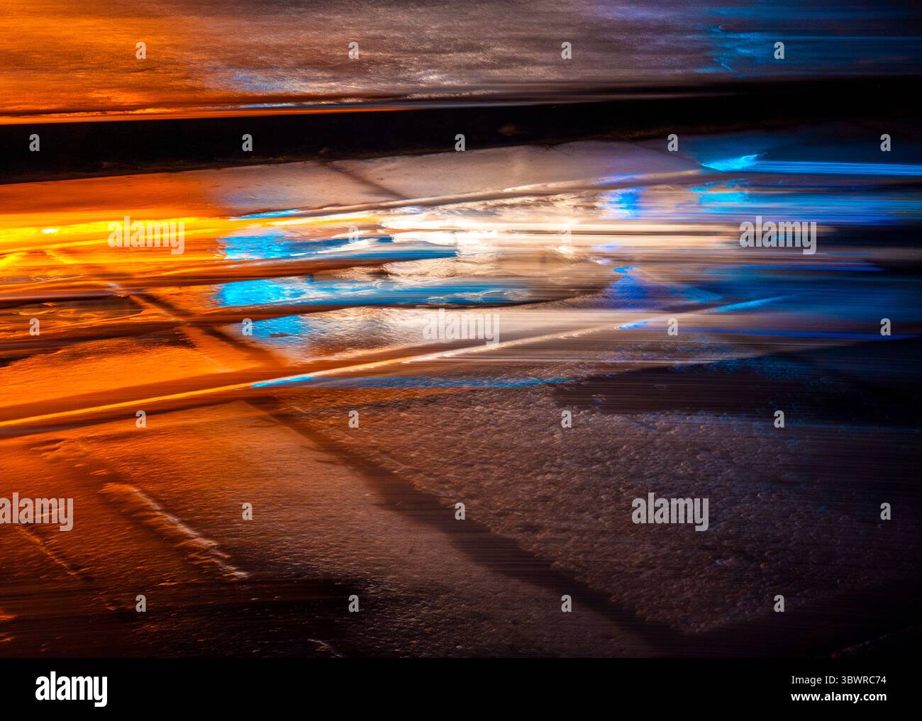 Sentieri di luce colorata che intrecciano una composizione astratta su una strada asfaltata bagnata di notte, creando una dinamica scena urbana piena di energia vibrante Foto Stock