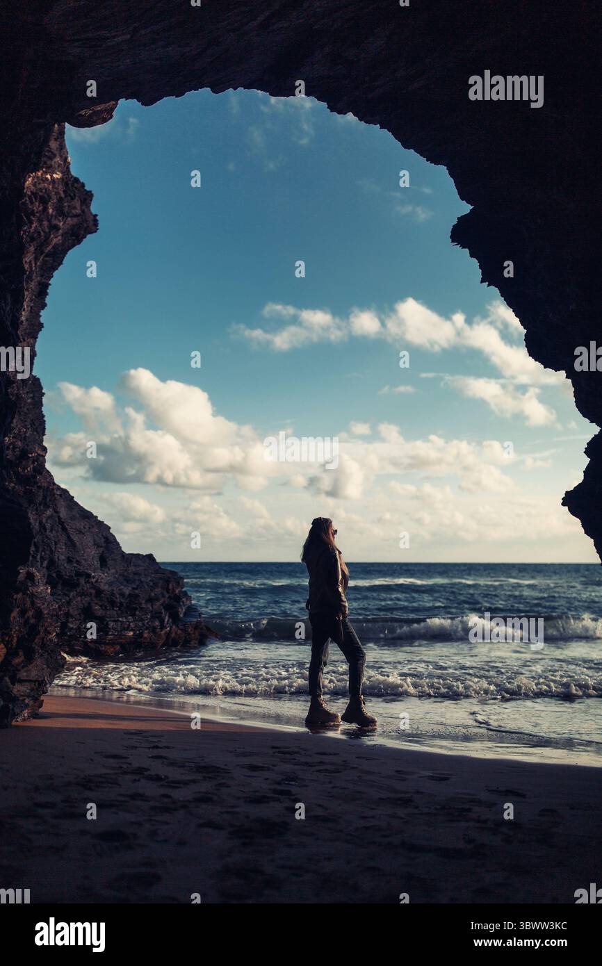 Una donna si trova all'ingresso di una grotta sul mare Foto Stock