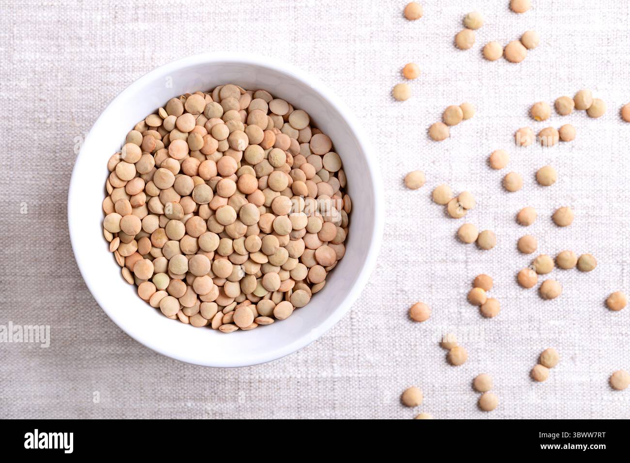 Lastre di lenticchie in una ciotola bianca su tessuto di lino. Ampia varietà di lenticchie verdi, non sgusciate, secche, tipicamente di forma piatta, che mantengono la loro forma quando cucinate. Foto Stock
