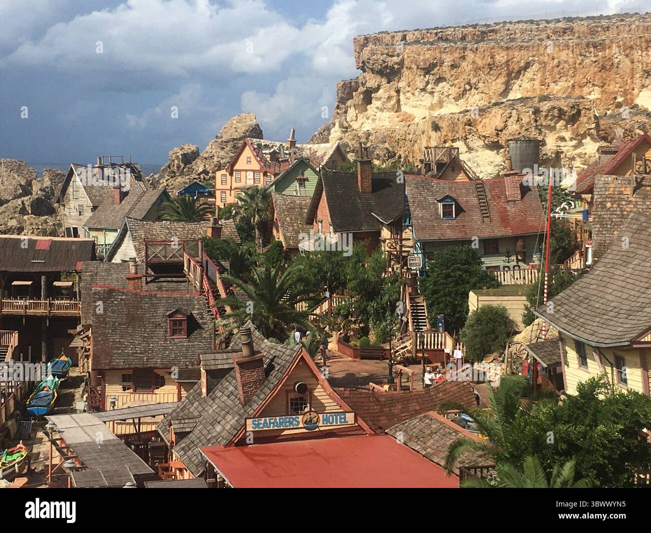 Set cinematografico del villaggio di braccio di ferro e scene di parco divertimenti, con vivaci case in legno, oggetti di scena e la costa di Anchor Bay sotto la luce del Mediterraneo. Foto Stock