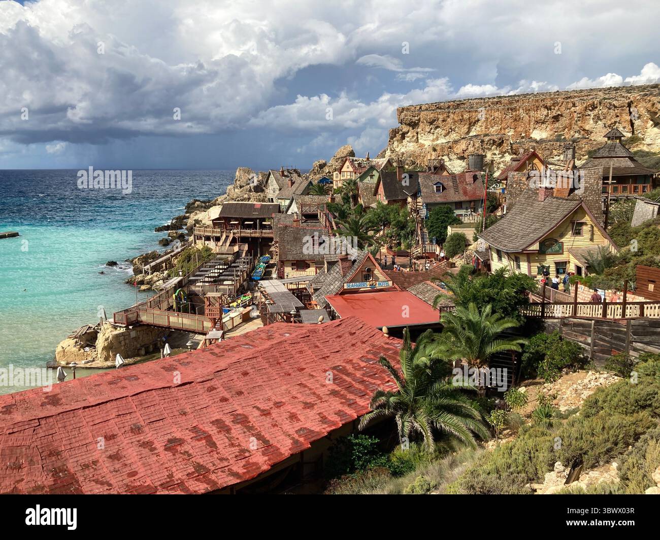 Iconico set cinematografico del villaggio di braccio di ferro e scene di parco divertimenti, con vivaci case in legno, oggetti di scena e la costa di Anchor Bay sotto il giglio del Mediterraneo Foto Stock
