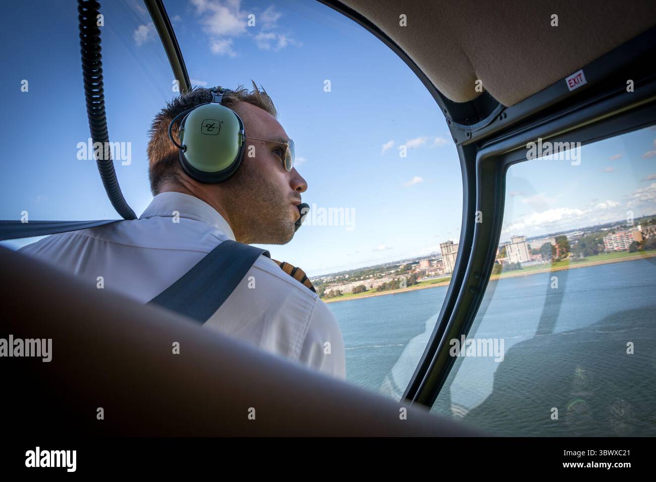 Pilota di elicottero a bordo di un elicottero Robinson R44 che guarda fuori dal finestrino laterale mentre gira in acqua aperta durante il volo. Foto Stock