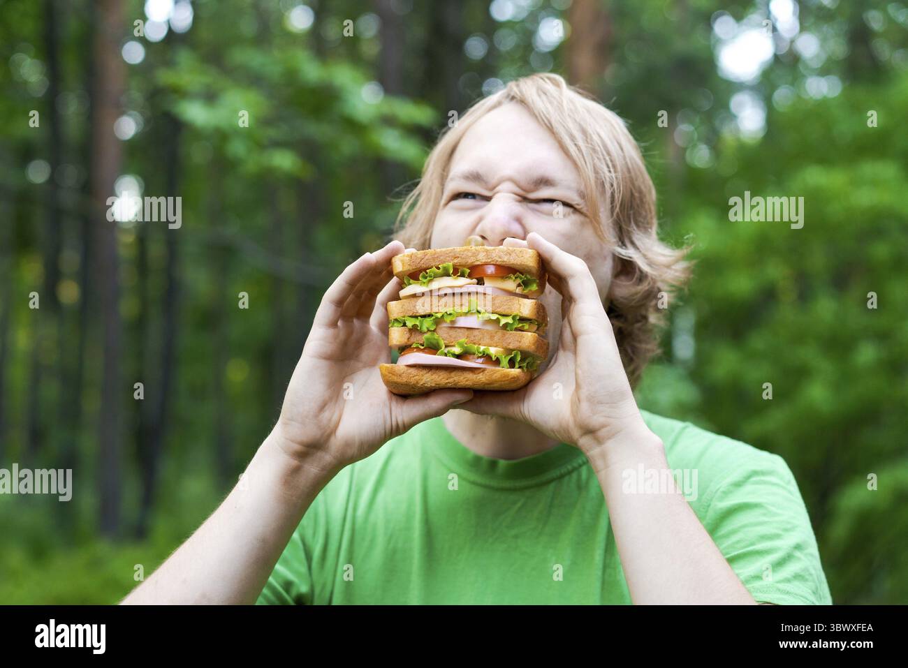 Giovane che tiene un pezzo di panino grande salsiccia sul piatto. Lo studente mangia fast food Foto Stock