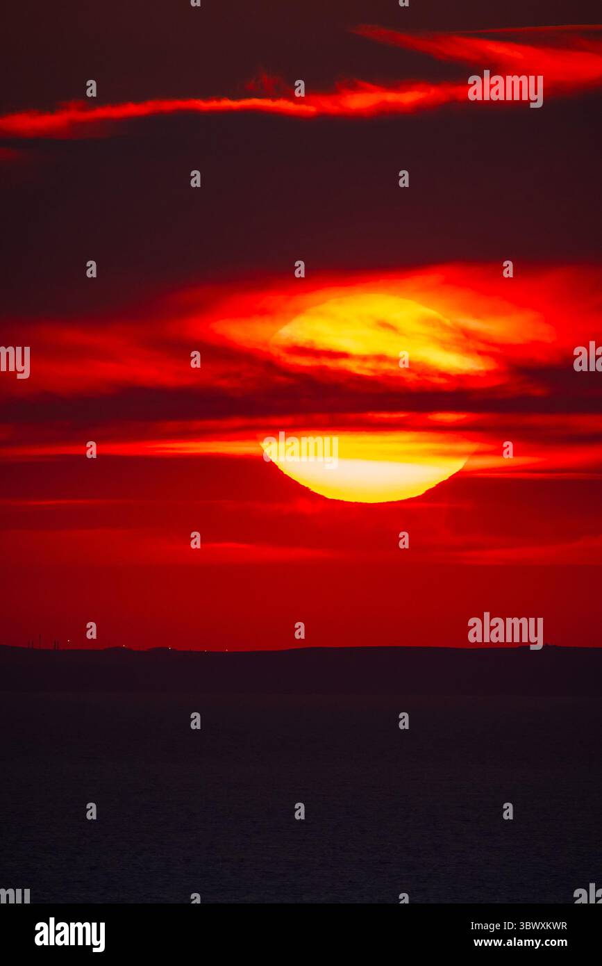 Tramonto rosso sull'orizzonte del mare con una silhouette scura di colline lontane. Foto Stock