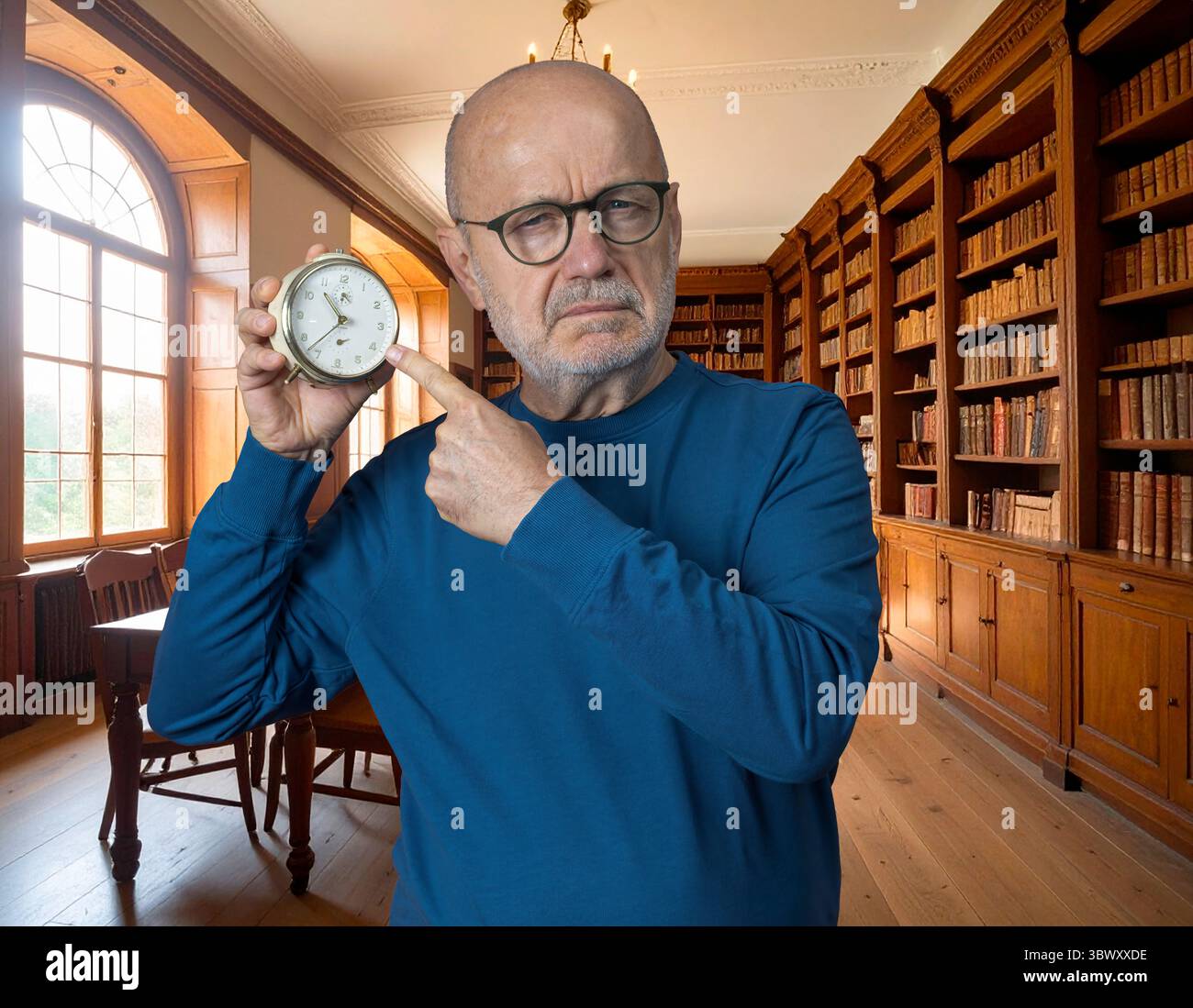 un uomo mostra una vecchia sveglia in mano in un'antica biblioteca Foto Stock