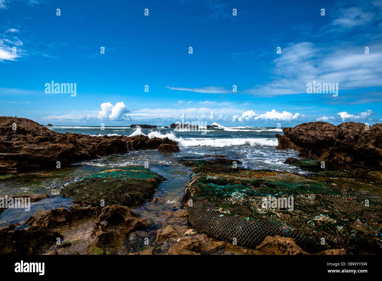 Le rocce intorno alla città di Essaouira proteggono la città marocchina dall'Oceano Atlantico tra cieli blu e nuvole bianche Foto Stock