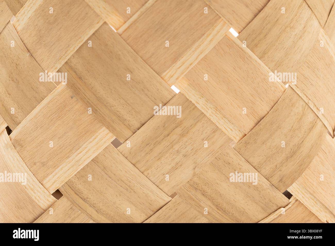 La tessitura intricata di strisce di legno crea un motivo naturale con trama. La luce mette in risalto la maestria artigianale, sottolineando la bellezza organica dei materiali utilizzati in questo design dettagliato. Foto Stock