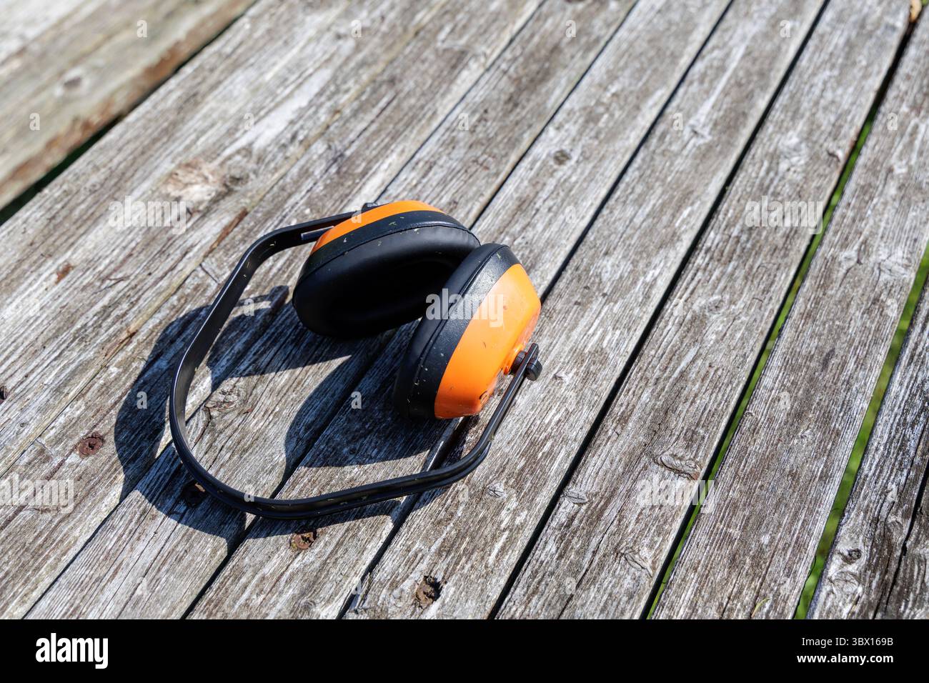 Le cuffie di protezione dell'udito arancione brillante e nero poggiano su tavole di legno intemperie, a indicare la sicurezza o i lavori all'aperto. Foto Stock