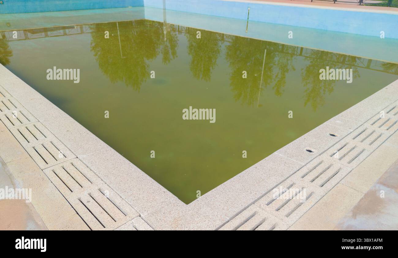 Grande piscina mezza vuota con acqua piena di alghe. Lavaggio a secco in piscina, sole, nessuno Foto Stock