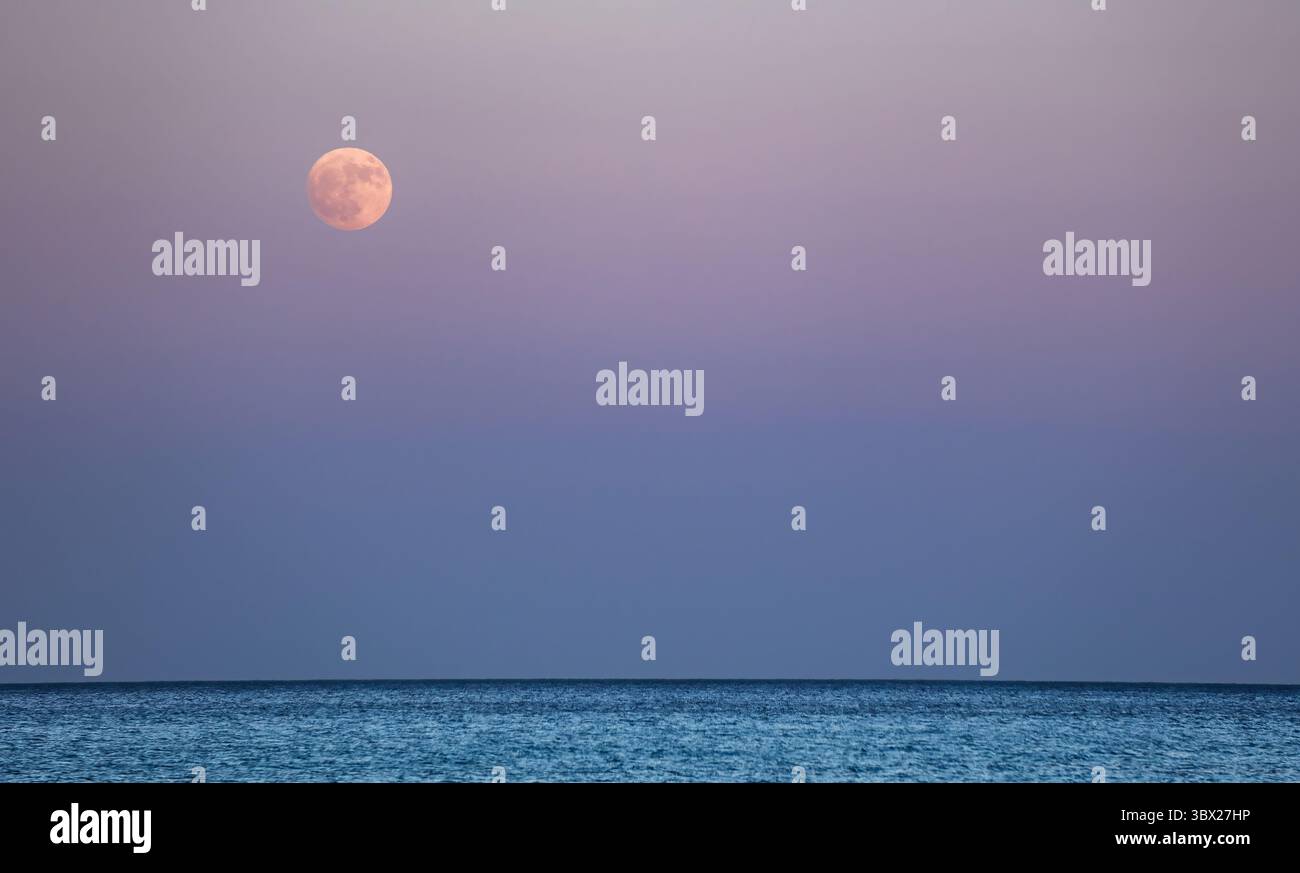 Una grande luna è nel cielo sopra un mare Egeo calmo, in Grecia. Il cielo è di colore blu intenso con un tocco di viola. La luna è l'obiettivo principale dell'imag Foto Stock