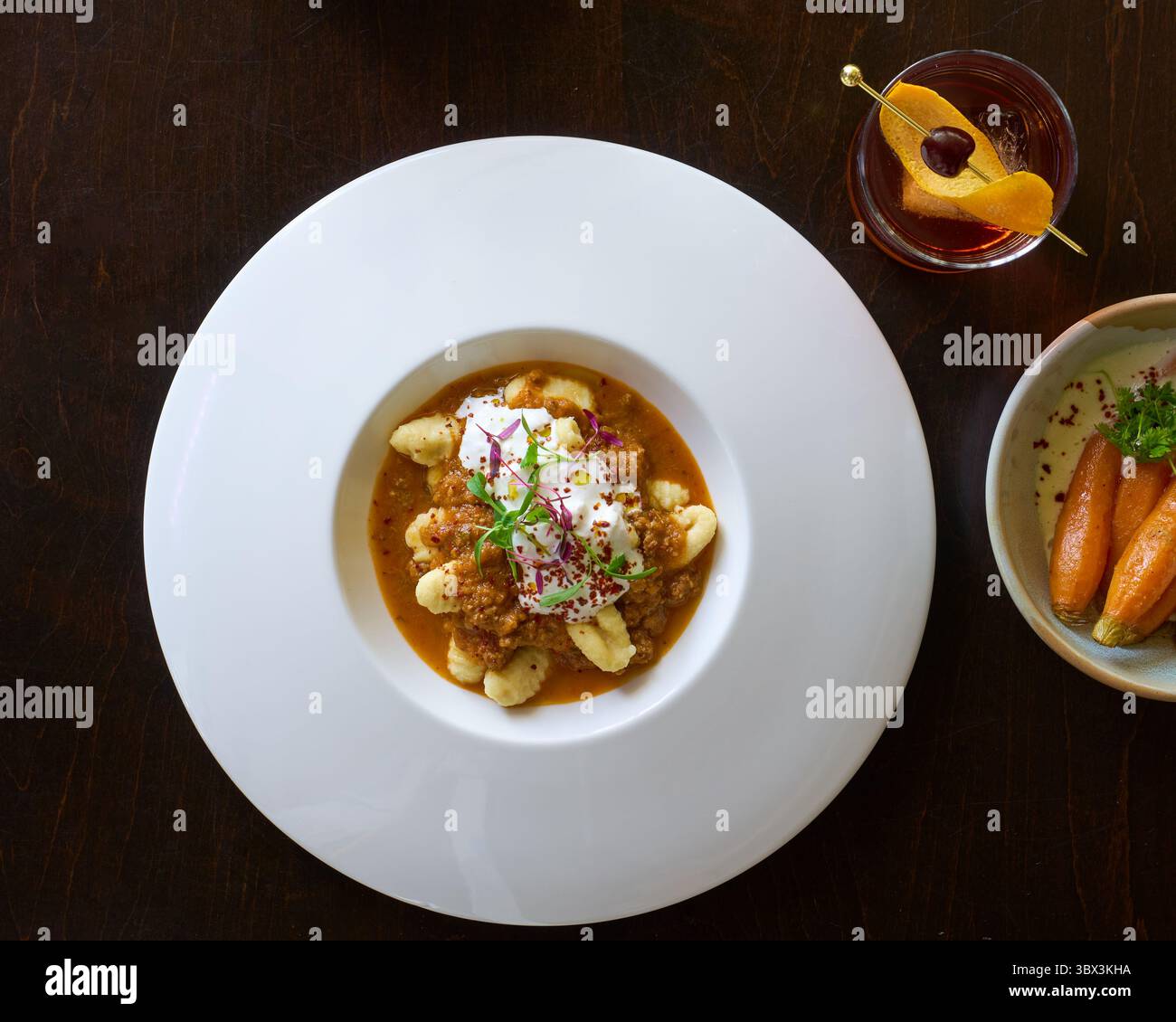 Gnocchi, salsa marrone, microverdi, formaggio grattugiato, piatto bianco, cene raffinate, presentazione del ristorante, cocktail abbinati, buccia d'arancia, ciliegina. Foto Stock