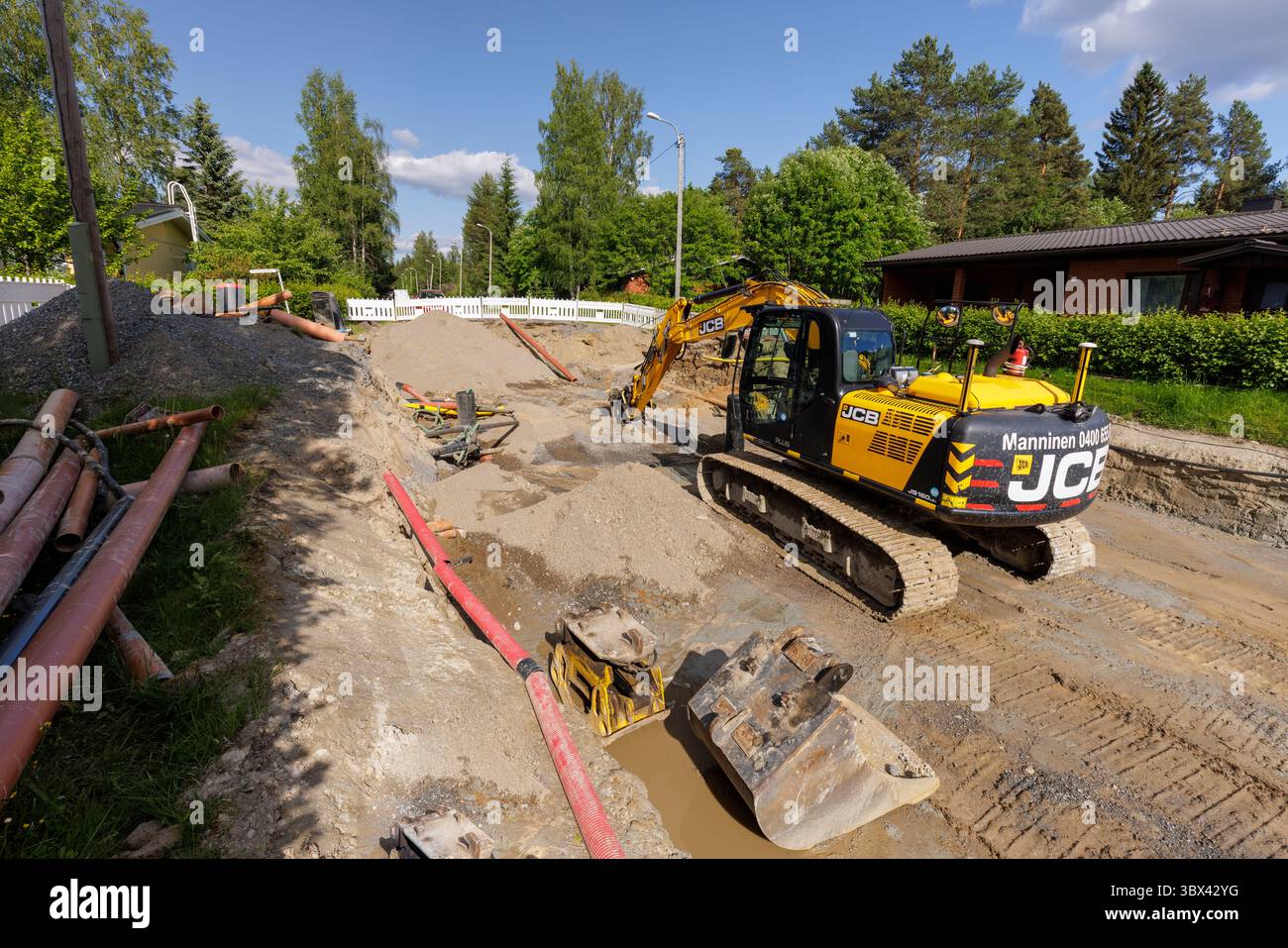 Scavatore JCB in trincea . Scavando la strada del sobborgo per nuove condotte idriche/fognarie , Finlandia Foto Stock