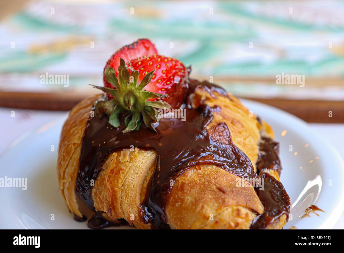 L'immagine mostra un croissant dorato e friabile, generosamente ricoperto da una salsa di cioccolato fondente lucida che gocciola giù per le pieghe Foto Stock