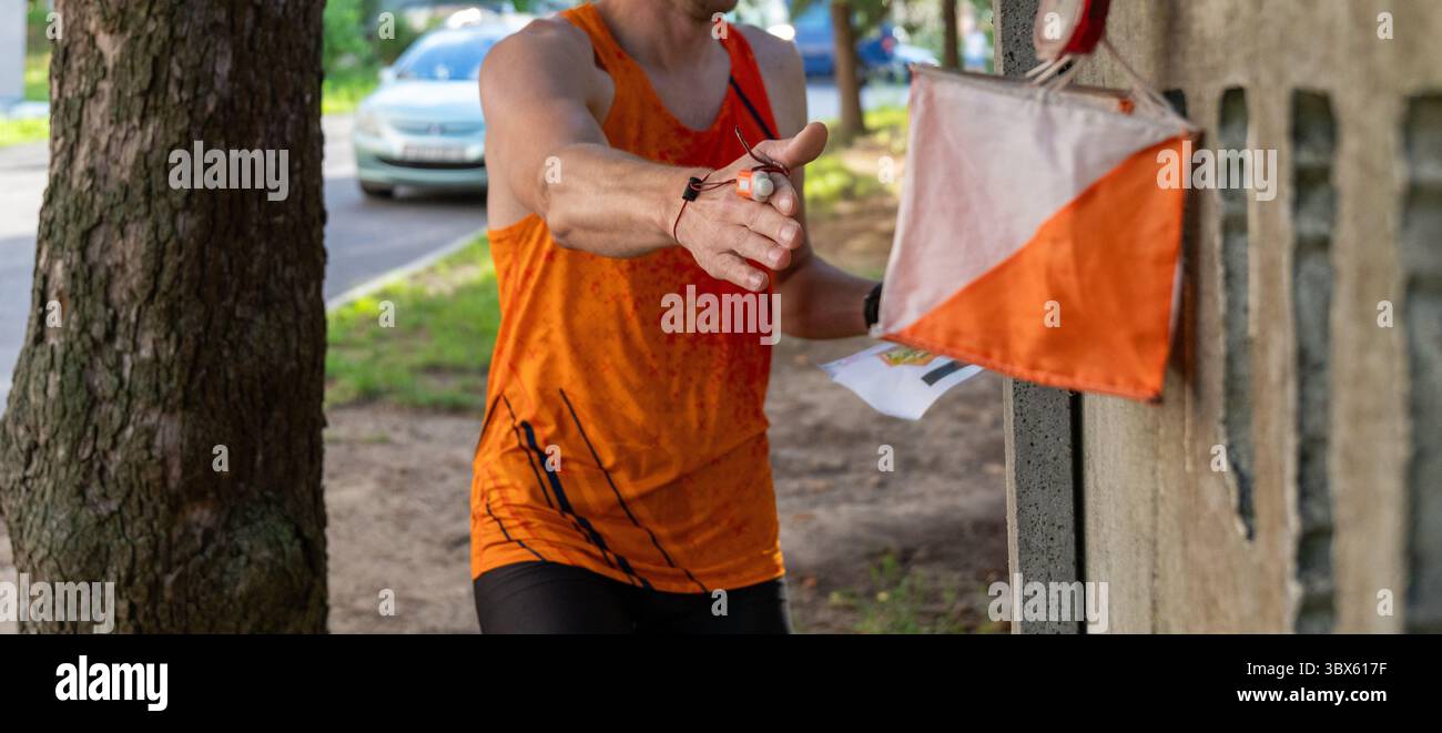 Un atleta in orientamento stradale registra un punto di controllo con un chip elettronico al dito. Il marcatore a prisma è montato su una recinzione in calcestruzzo d Foto Stock