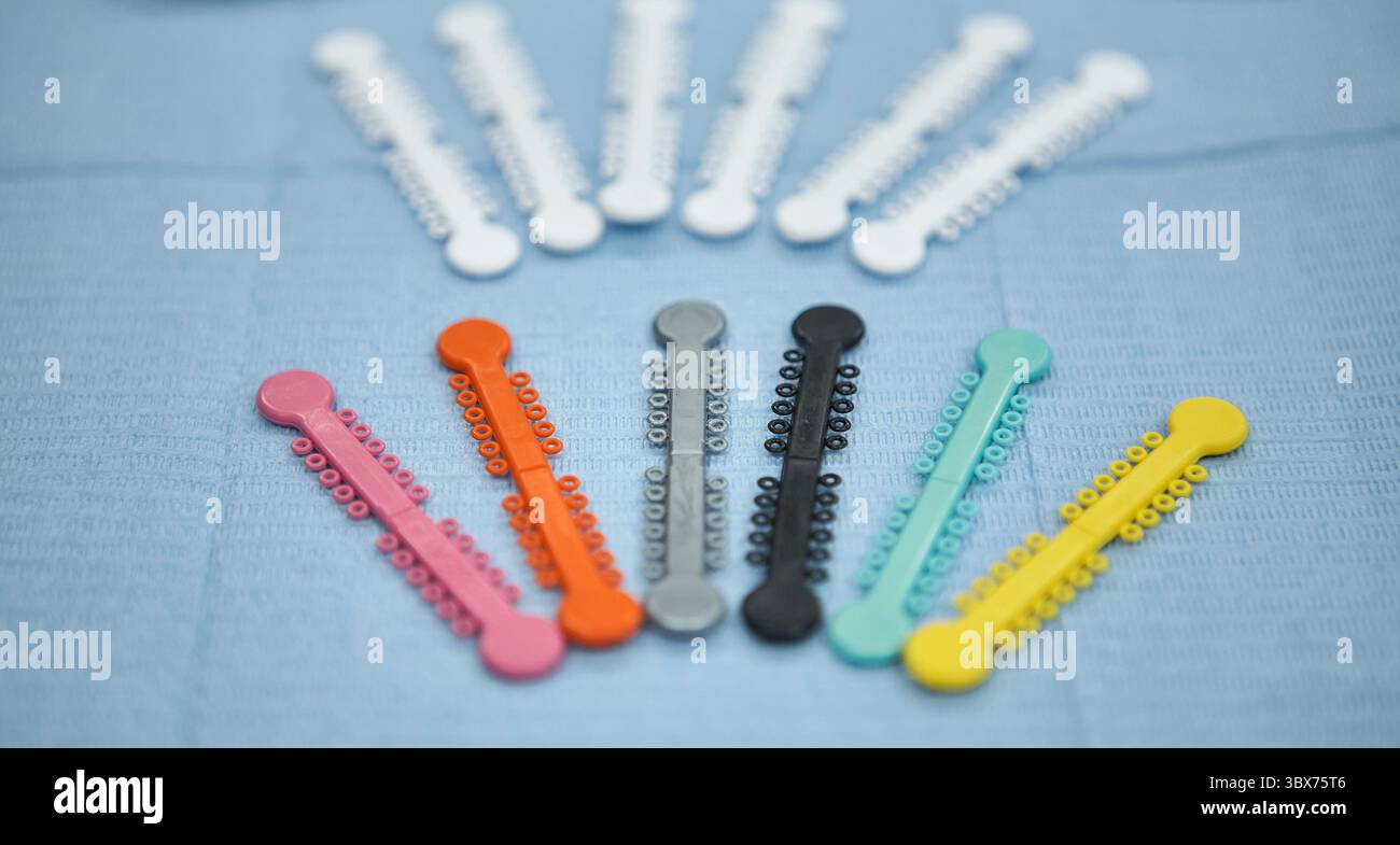 Immagine ravvicinata di legature ortodontiche multicolore disposte a semicerchio su un panno dentale blu testurizzato. Queste fasce elastiche sono utilizzate in o. Foto Stock
