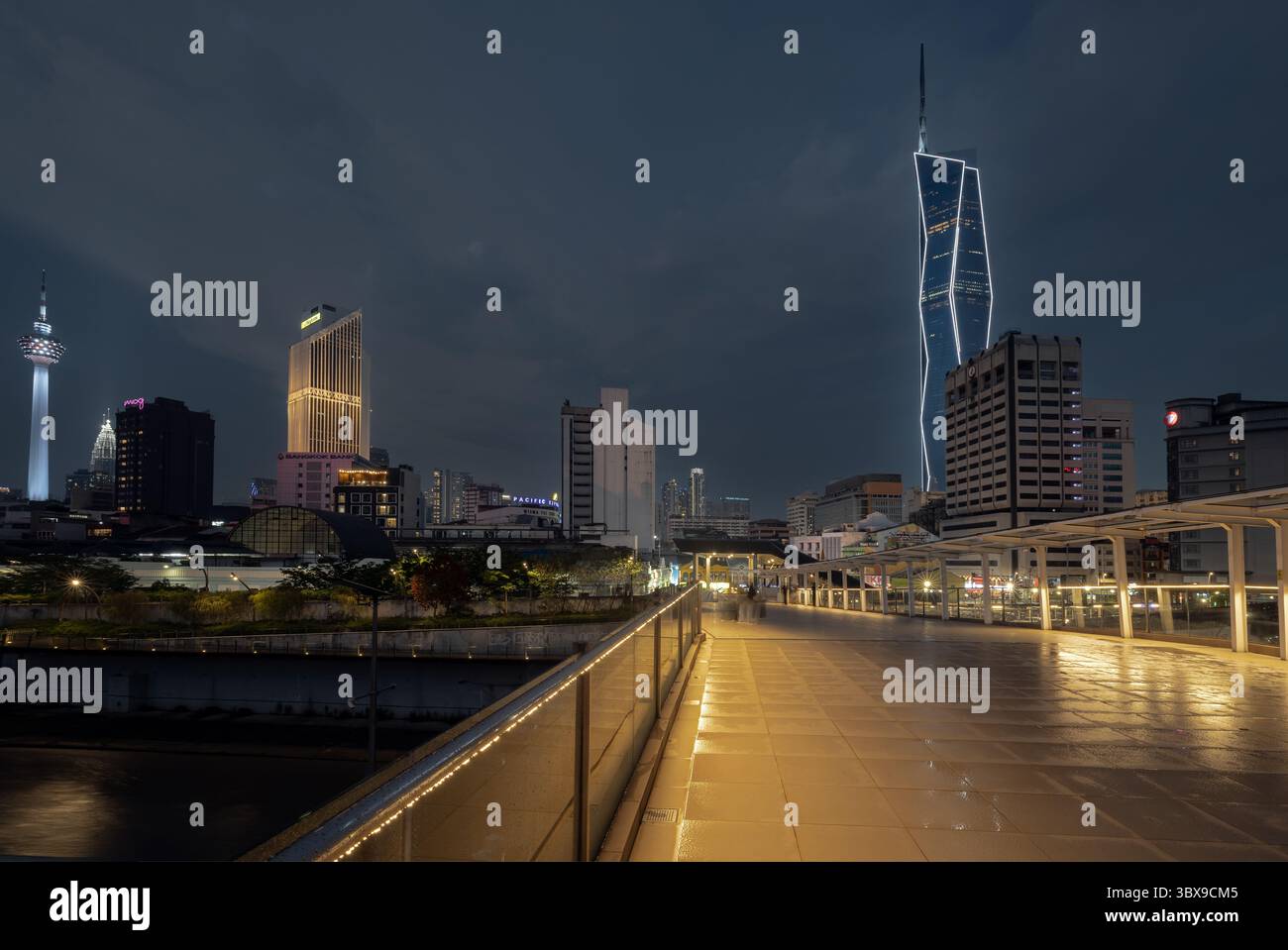 Vista notturna dal ponte pedonale alla stazione LRT di Masjid Jamek nel centro di Kuala Lumpur con grattacielo Merdeka 118 illuminato sullo sfondo Foto Stock