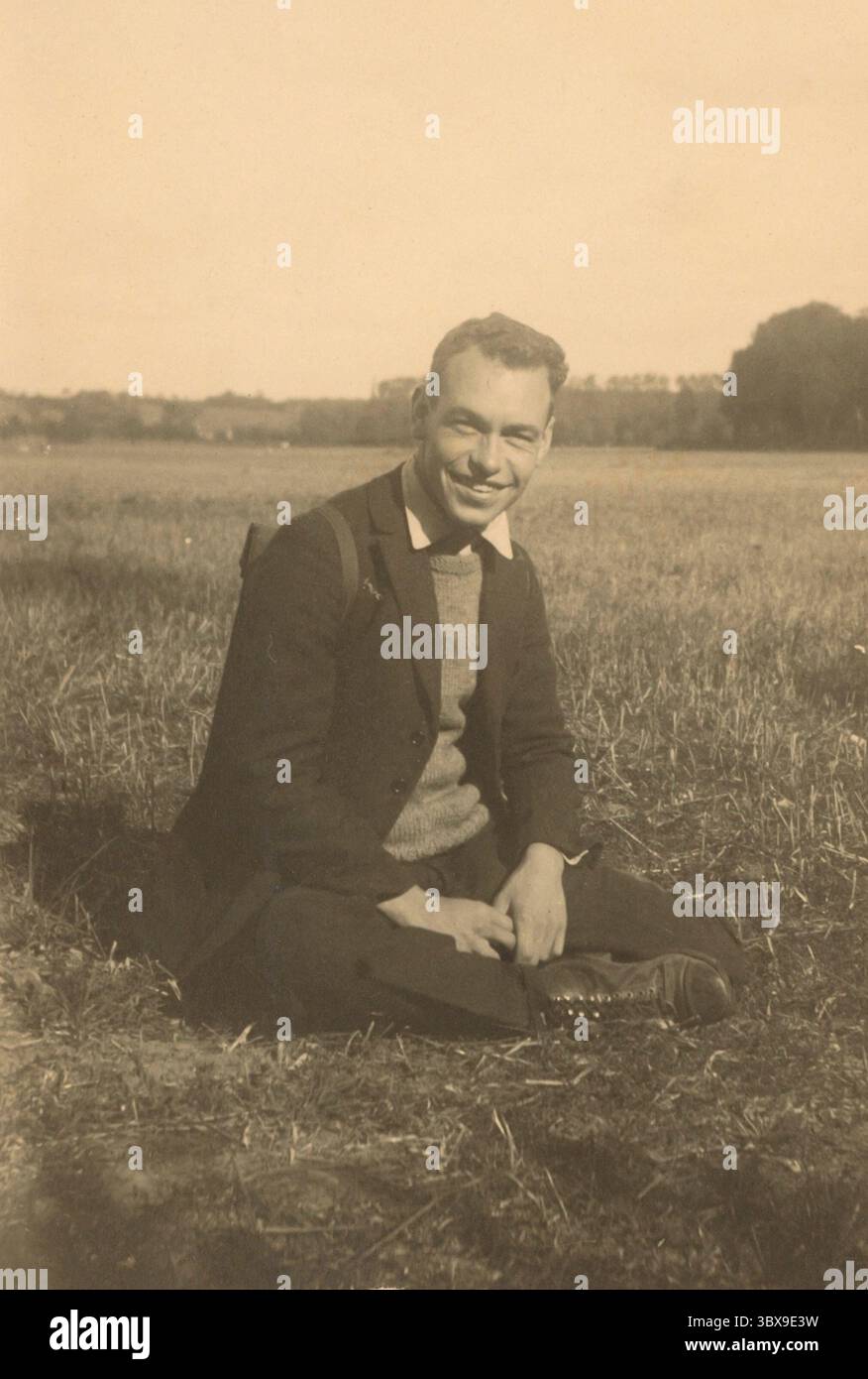 Foto storica d'epoca dell'artista Thomas Handforth seduto in un campo, indossando un maglione e un cappotto. Presa nel 1921. Foto Stock