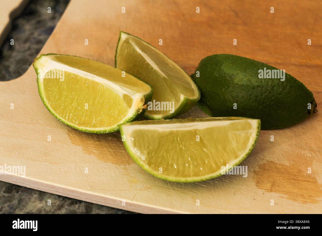 Primo piano di spicchi di lime tagliati a fette su un tagliere in legno Foto Stock