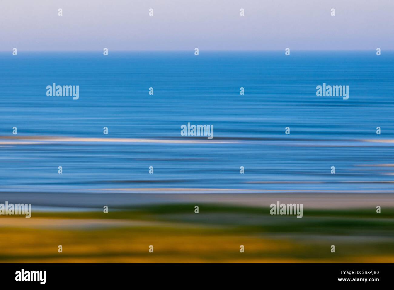 I tenui colori pastello si fondono perfettamente in una scena oceanica sfocata, creando linee orizzontali astratte mentre le onde rotolano dolcemente verso la riva al crepuscolo Foto Stock