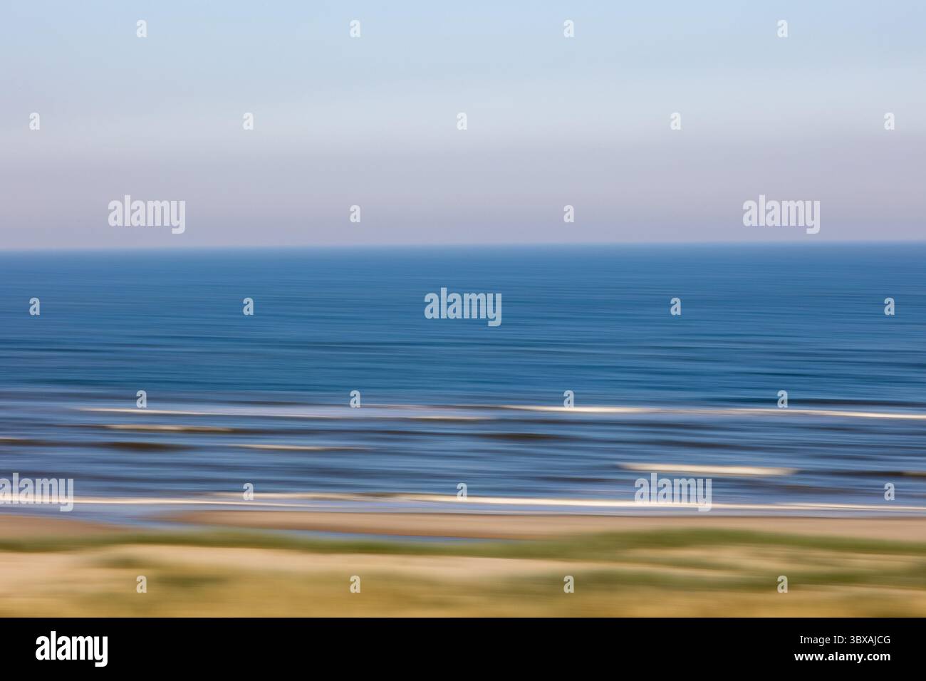 I tenui colori pastello si fondono perfettamente in una scena oceanica sfocata, creando linee orizzontali astratte mentre le onde rotolano dolcemente verso la riva al crepuscolo Foto Stock