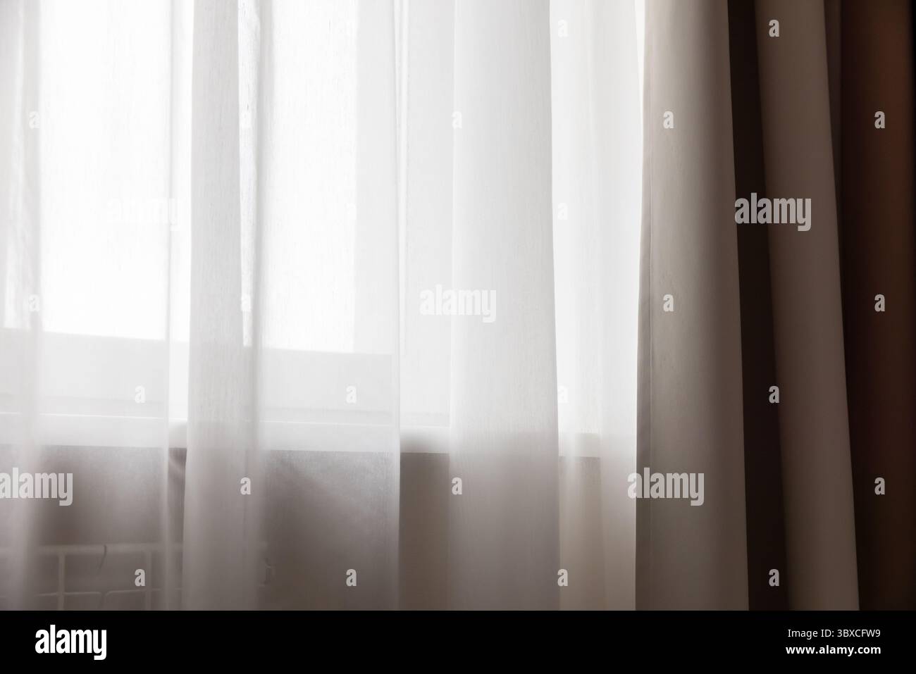 Le eleganti tende bianche trasparenti sono appese graziosamente, diffondendo delicatamente la luce naturale in una sala serena e minimalista. Rappresentazione perfetta di calma, pace, AN Foto Stock