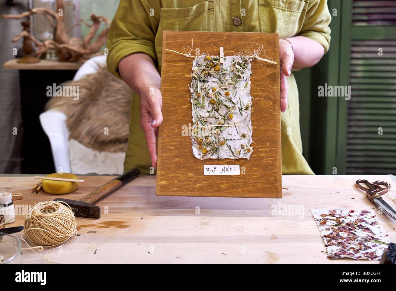 Donna che tiene in mano un pannello da parete finito in carta floreale fatta a mano su legno. Artigianato ecologico con materiali naturali e messaggio positivo: "Perché no? Foto Stock Donna che tiene in mano un pannello da parete finito in carta floreale fatta a mano su legno. Artigianato ecologico con materiali naturali e messaggio positivo: "Perché no? Foto Stock