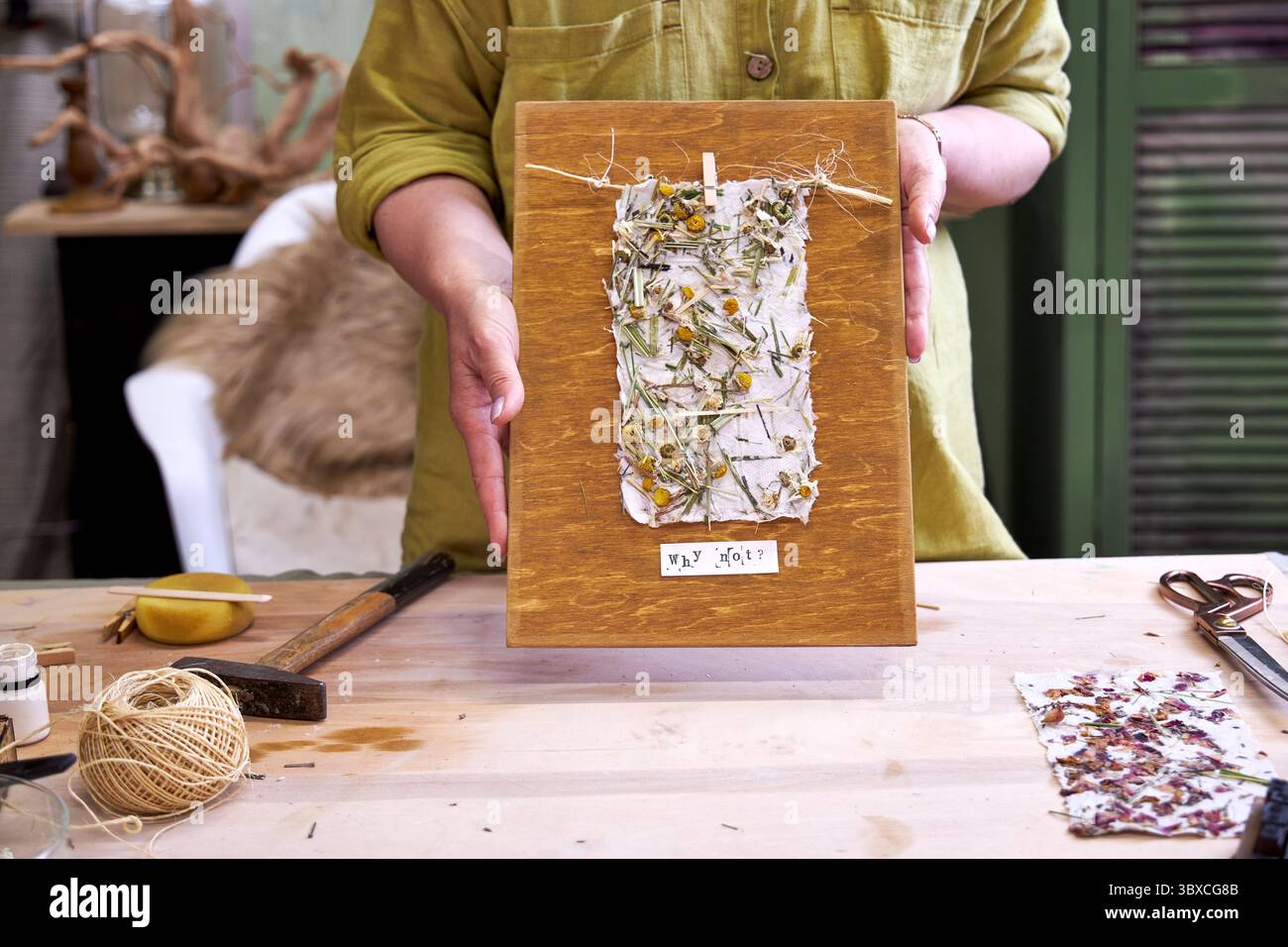 Donna che tiene in mano un pannello da parete finito in carta floreale fatta a mano su legno. Artigianato ecologico con materiali naturali e messaggio positivo: "Perché no? Foto Stock Donna che tiene in mano un pannello da parete finito in carta floreale fatta a mano su legno. Artigianato ecologico con materiali naturali e messaggio positivo: "Perché no? Foto Stock