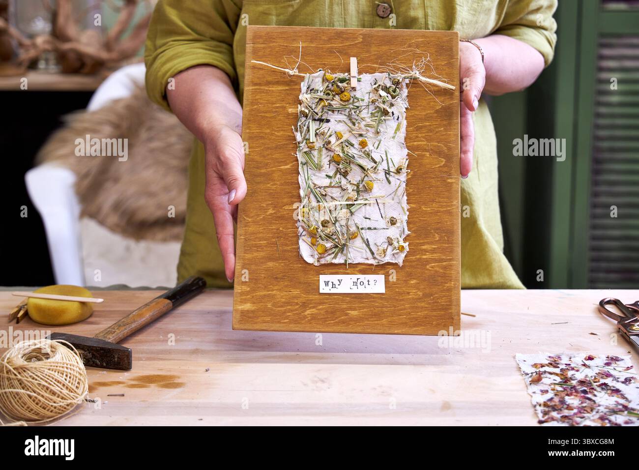 Donna che tiene in mano un pannello da parete finito in carta floreale fatta a mano su legno. Artigianato ecologico con materiali naturali e messaggio positivo: "Perché no? Foto Stock Donna che tiene in mano un pannello da parete finito in carta floreale fatta a mano su legno. Artigianato ecologico con materiali naturali e messaggio positivo: "Perché no? Foto Stock