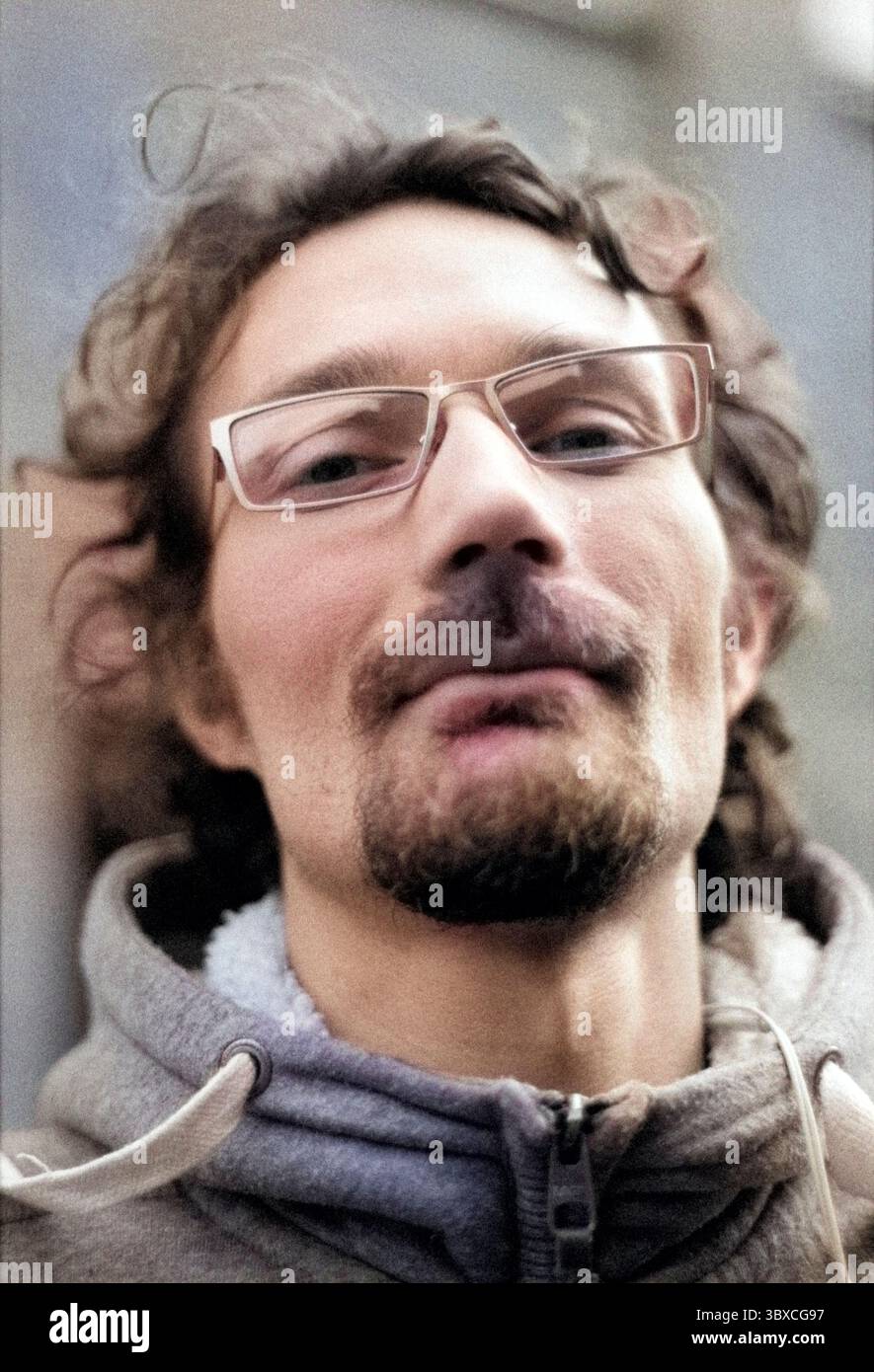 Ritratto in bianco e nero e foto della testa di un adulto, uomo caucasico che indossa gli occhiali e cammina per le strade del centro di Tilburg, Paesi Bassi. Ripresa su pellicola analogica e colorazione con filtri neurali ai / A.I. Adobe Photoshop PS. MR=SÌ Foto Stock