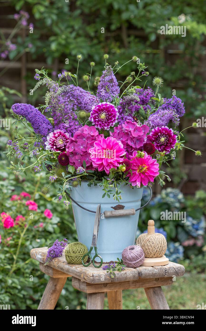 composizione floreale di dalie rosa, ortensie e fiori di cespuglio di farfalle in un vecchio secchio di smalto nel giardino estivo Foto Stock